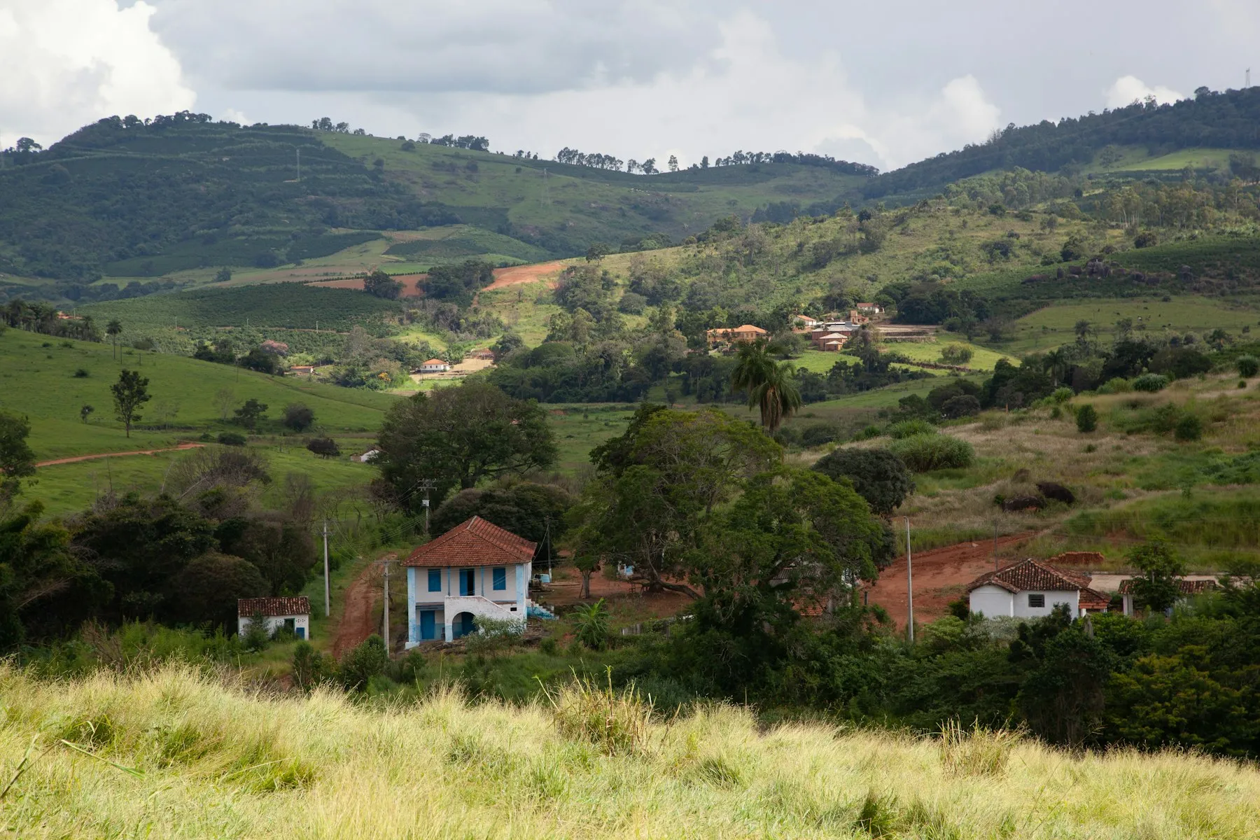 Sede de fazenda com casarão branco de janelas azuis entre pastos e morros